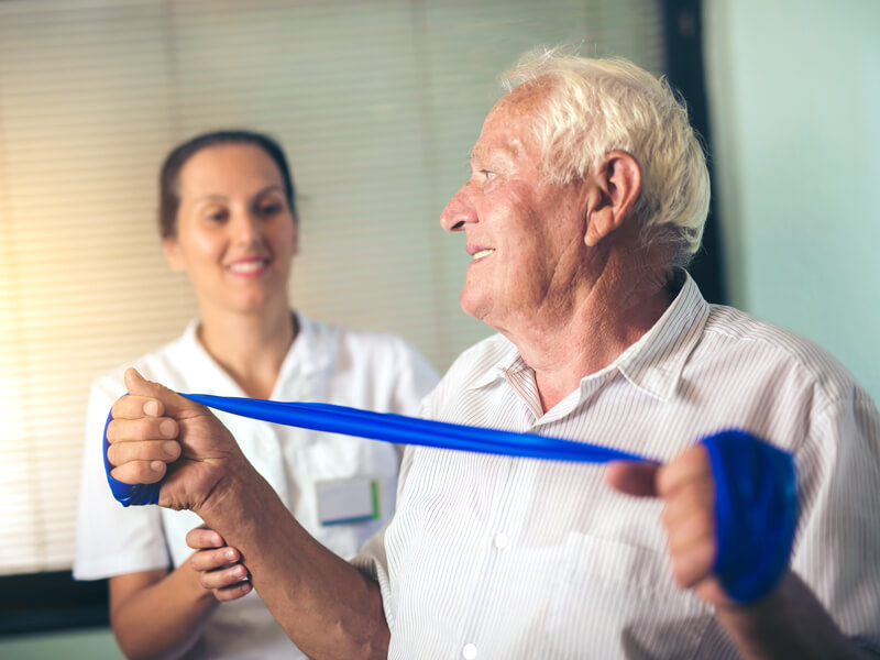 rehabilitation therapy nurse helping elderly man exercise with tension strap